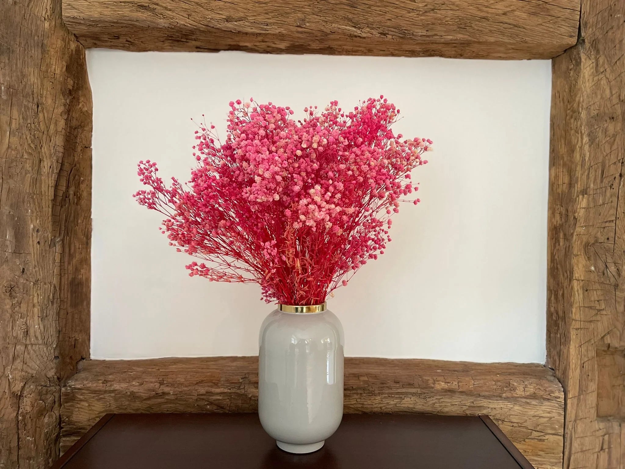 Getrocknetes Schleierkraut in Rosa in einer hellen Vase vor Holzbalken
